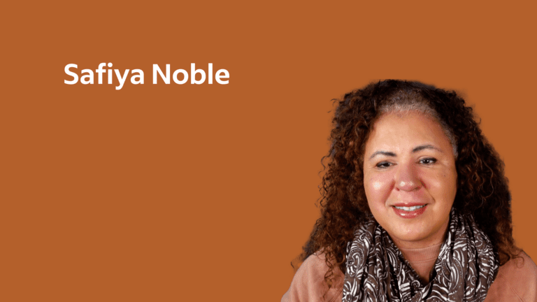 Dr Noble has shoulder length curly hair. Safiya wears a salmon colored top and a brown patterned scarf. She appears on a terracotta background.